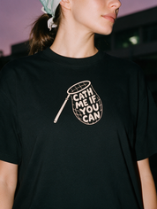 Woman photographed with flash at night, wearing a black cotton T-shirt with a butterfly net design lettered 'CATH ME IF YOU CAN'