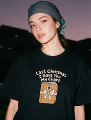 Woman photographed with flash at night, wearing a black cotton T-shirt printed "Last Christmas I Gave You My Chart" above a wrapped chart