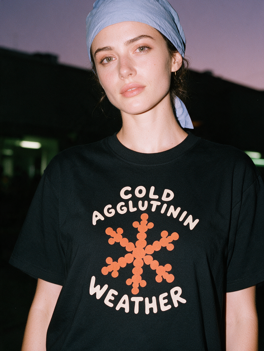 Woman photographed with flash at night, wearing a black cotton T-shirt with an orange snowflake and the text 'Cold Agglutinin Weather.'
