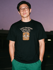 Man in glasses, photographed with flash at night, wearing a black cotton T-shirt printed "Last Christmas I Gave You My Chart" above a wrapped chart