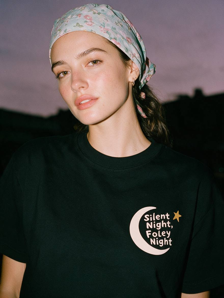Woman photographed with flash at night, wearing a black cotton T-shirt with a crescent moon, a star and 'Silent Night, Foley Night'
