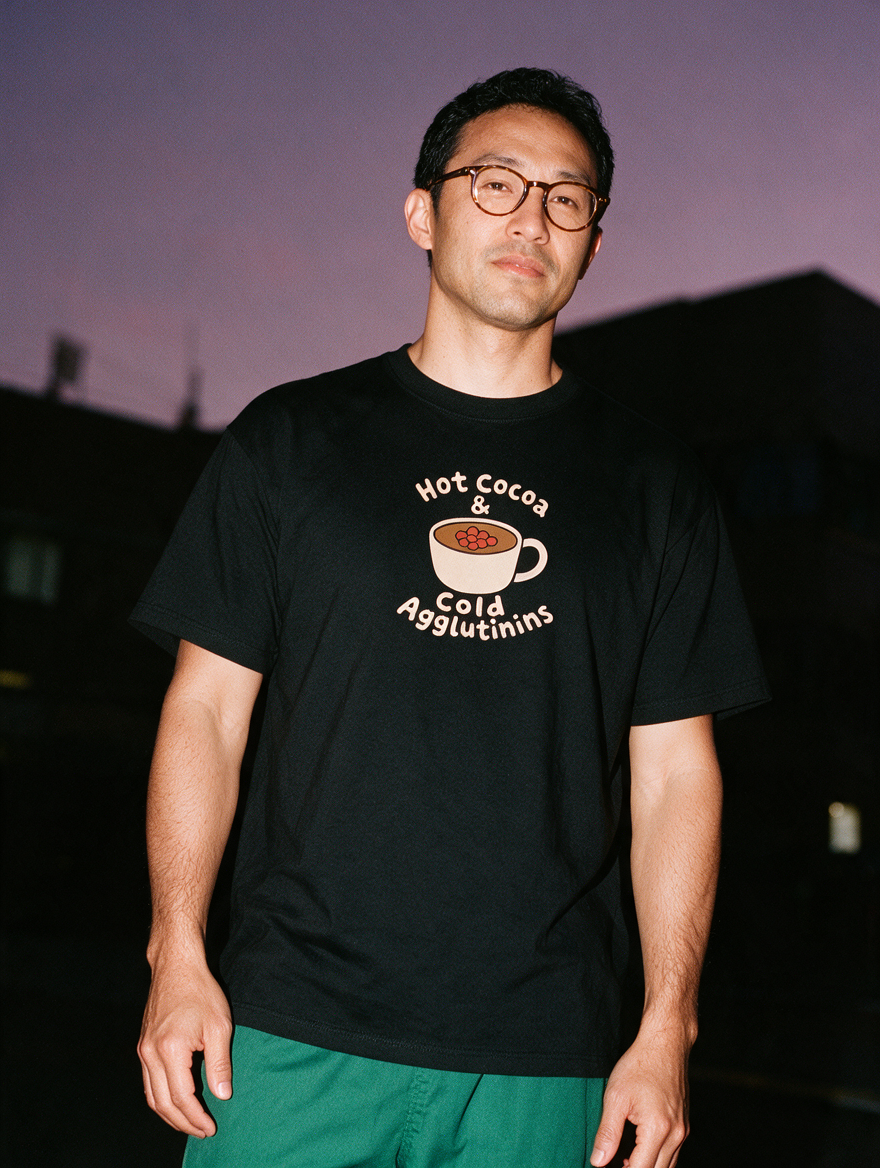 Man in glasses photographed with flash at night wearing a black cotton T-shirt with 'Hot Cocoa & Cold Agglutinins' around a mug of cocoa