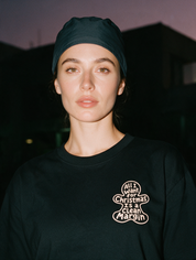 Woman in a scrub cap, photographed with flash at night, wearing a black cotton T-shirt with a small gingerbread print reading 'All I Want for Christmas Is a Clean Margin'