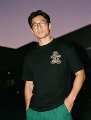 Man in round glasses, photographed with flash at night, wearing a black cotton T-shirt with a small gingerbread print reading 'All I Want for Christmas Is a Clean Margin'