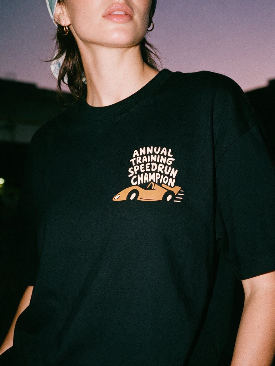Woman in a scrub cap, photographed with flash at night, wearing a black cotton T-shirt with 'Annual Training Speedrun Champion' and an orange race car.