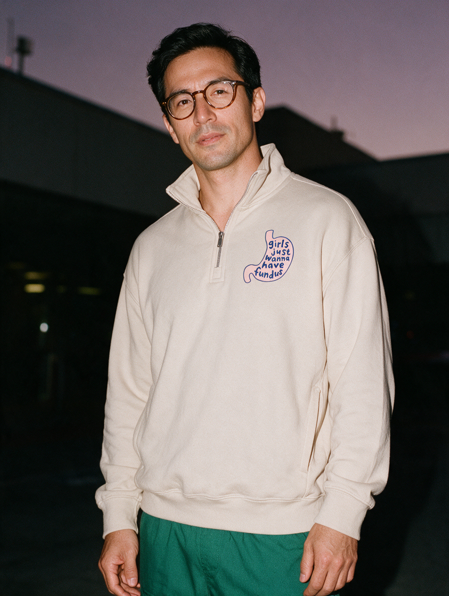 Man photographed with flash at night, wearing a light gray quarter-zip sweatshirt with the Girls Just Wanna Have Fundus design.